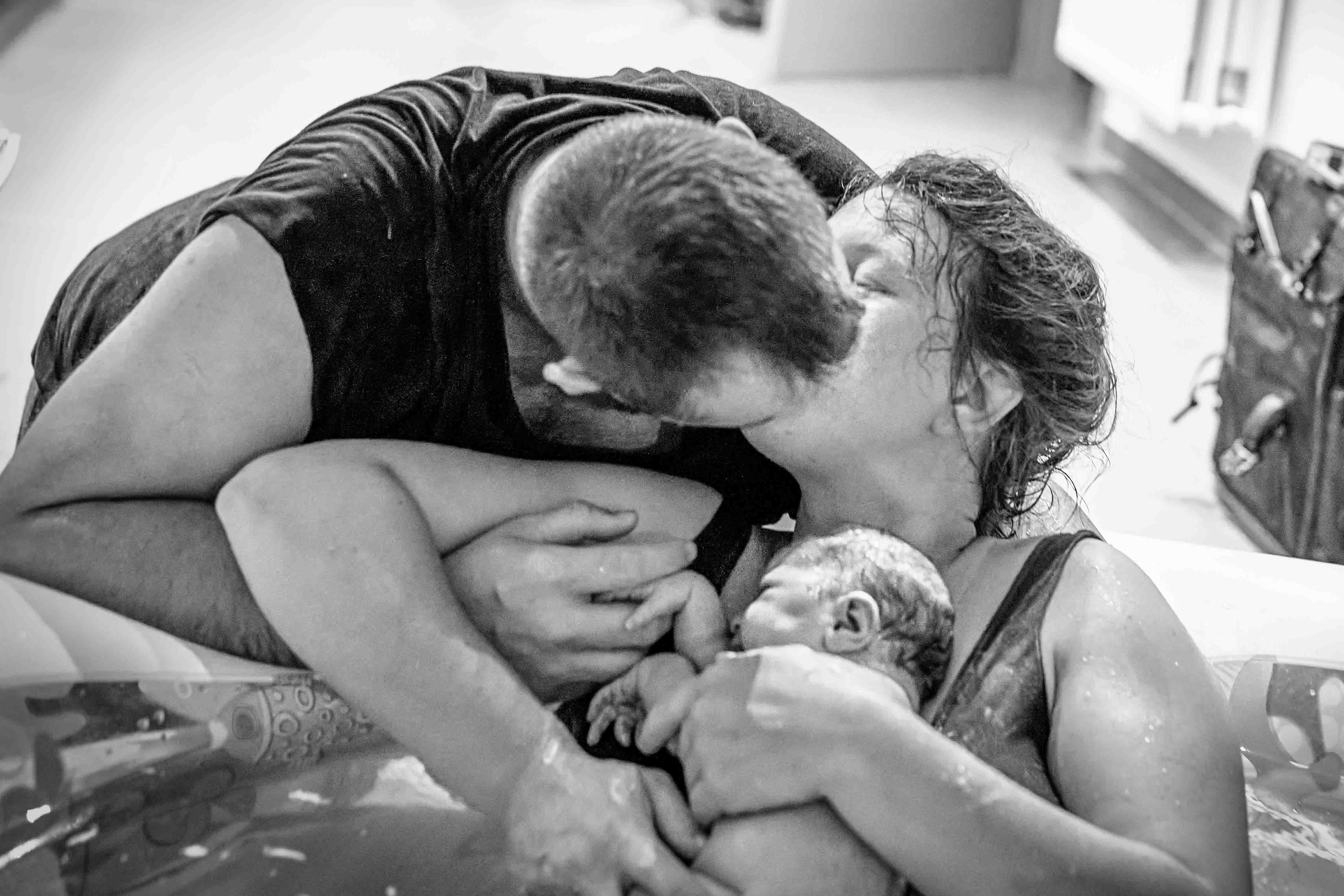 Man en vrouw kussen elkaar na de geboorte van hun baby die op de buik van de mama ligt